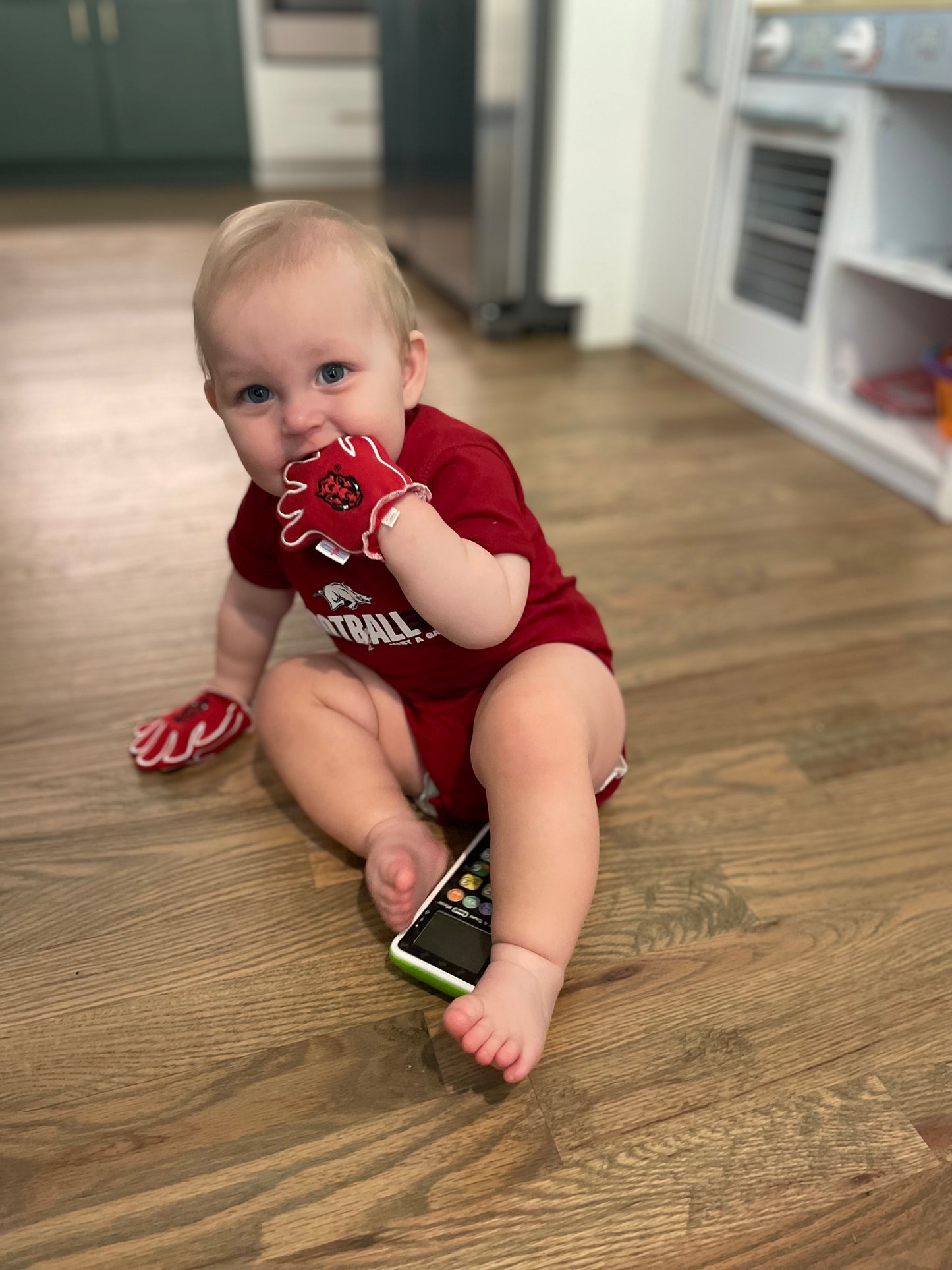 Baby wearing Arkansas Wooo Pig baby mittens in crimson