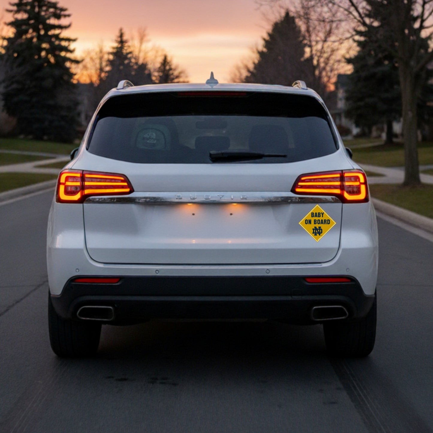 White SUV with a 'Baby on Board' sign at sunset