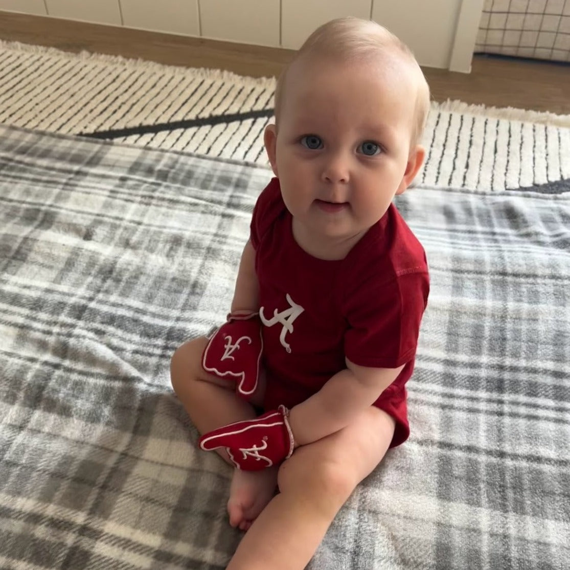 Infant wearing Alabama Roll Tide baby mittens in crimson