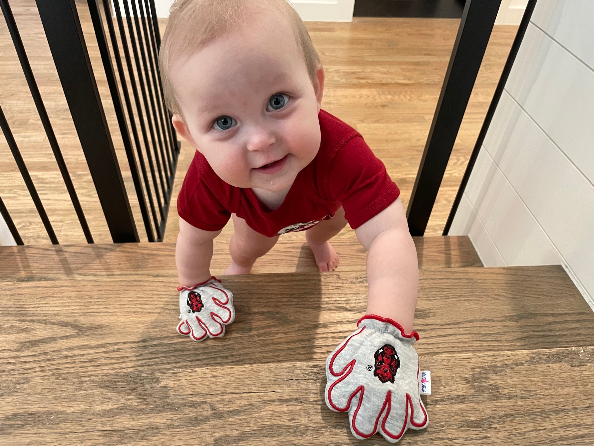 Baby wearing Arkansas Wooo Pig baby mittens in gray